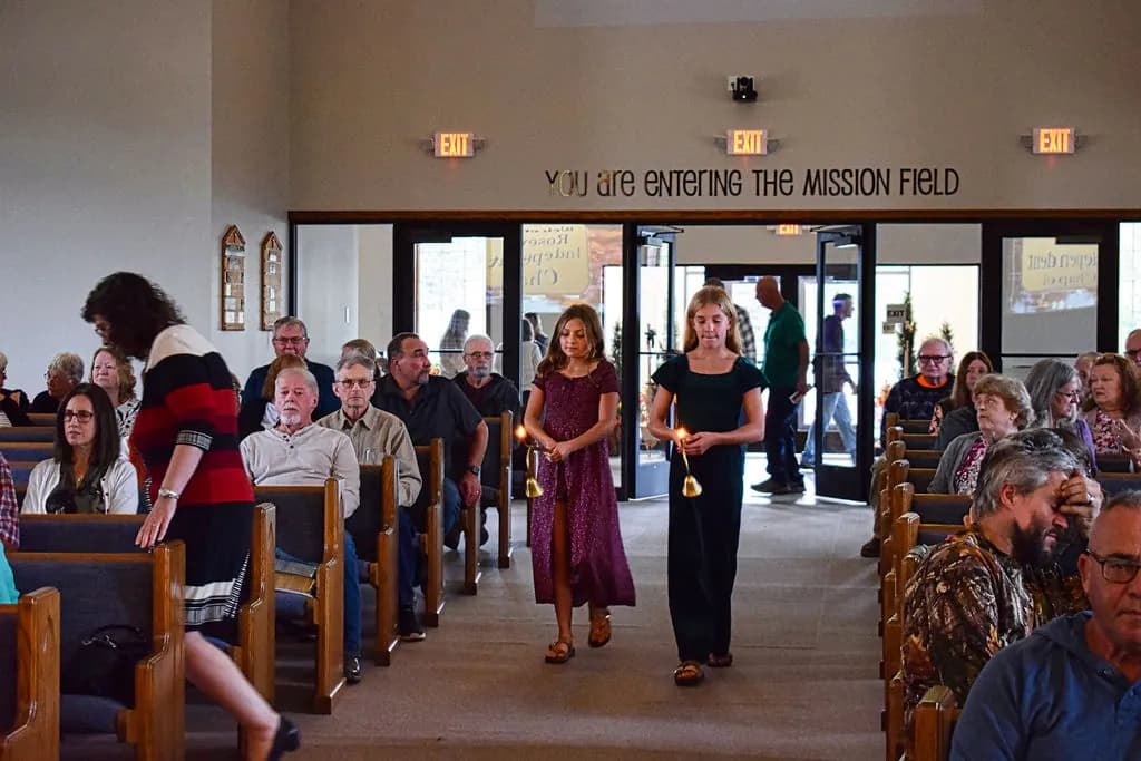 Two girls carrying the candle lighters down the center aisle beneath the words You are entering the mission field