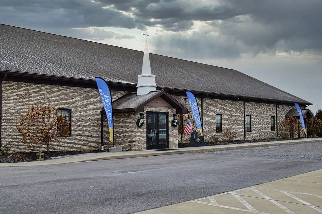 The original chapel and steeple on Route 322 under a broken sky, welcome banners along the lot