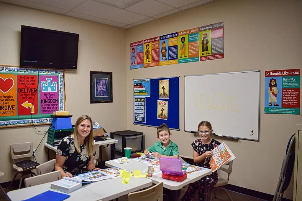 A Sunday School teacher smiling with two children at their table
