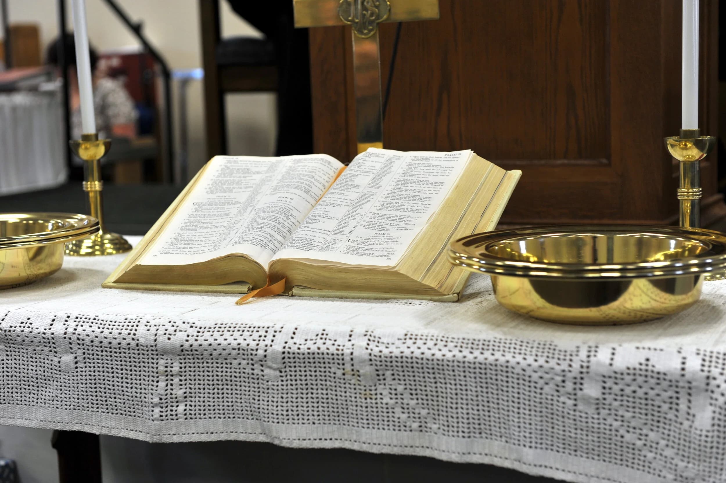An open Bible on the lace-covered table beside a brass offering plate and candlestick