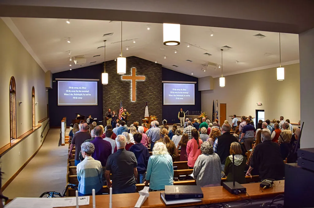 The congregation standing to sing in the new sanctuary, the lit cross and lyrics on the screens ahead