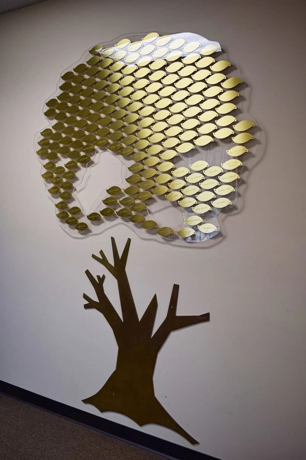 A wall of small brass fish, each one lettered, mounted above a tree of branches