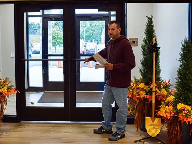 A greeter with bulletins in hand at the front doors of Roseville Independent Chapel, fall flowers on either side