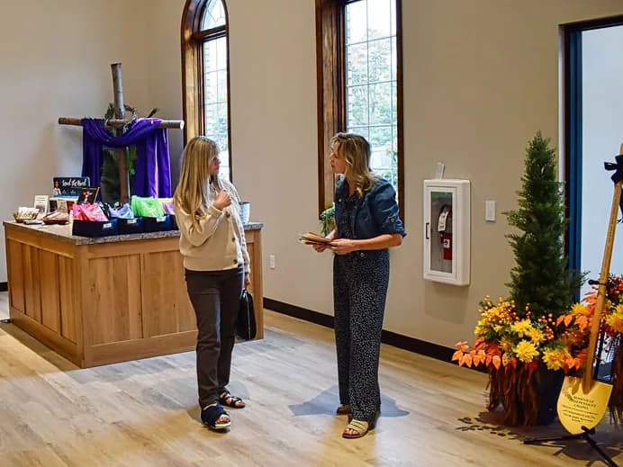 Two women talking in the lobby beside the welcome table and a draped wooden cross