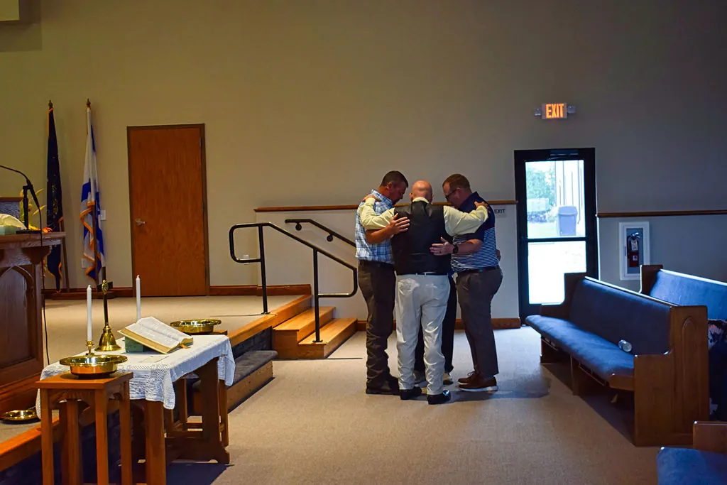 Men of the church with their arms around one another in prayer at the front of the sanctuary