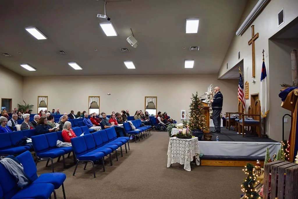 The sanctuary from the back during a service, blue chairs filled and the pastor at the front