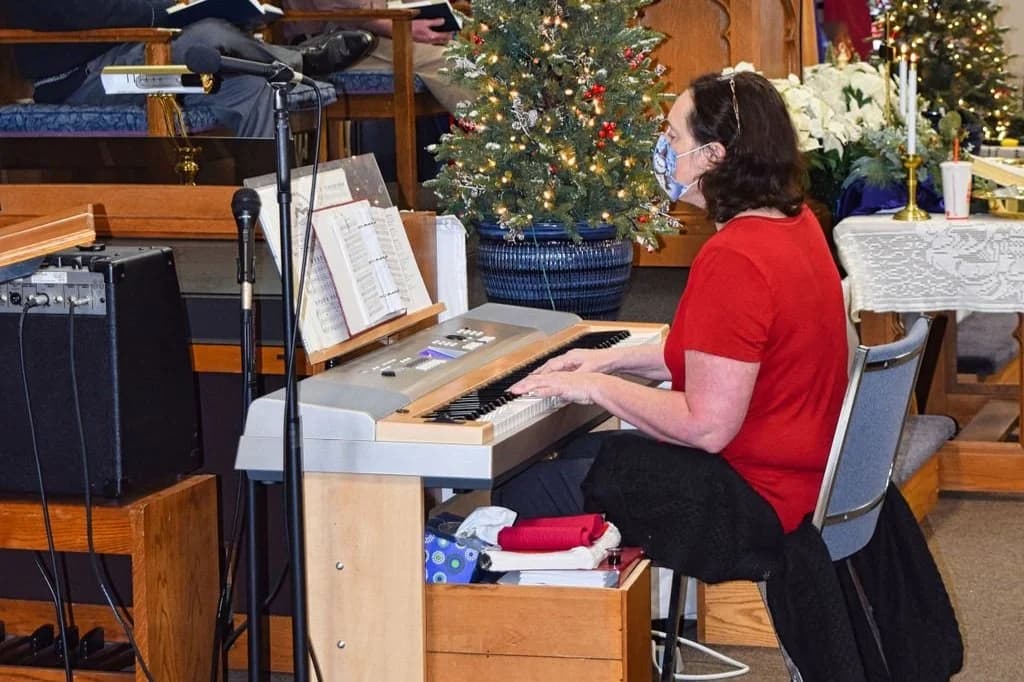 A pianist accompanying the singing beside a decorated Christmas tree
